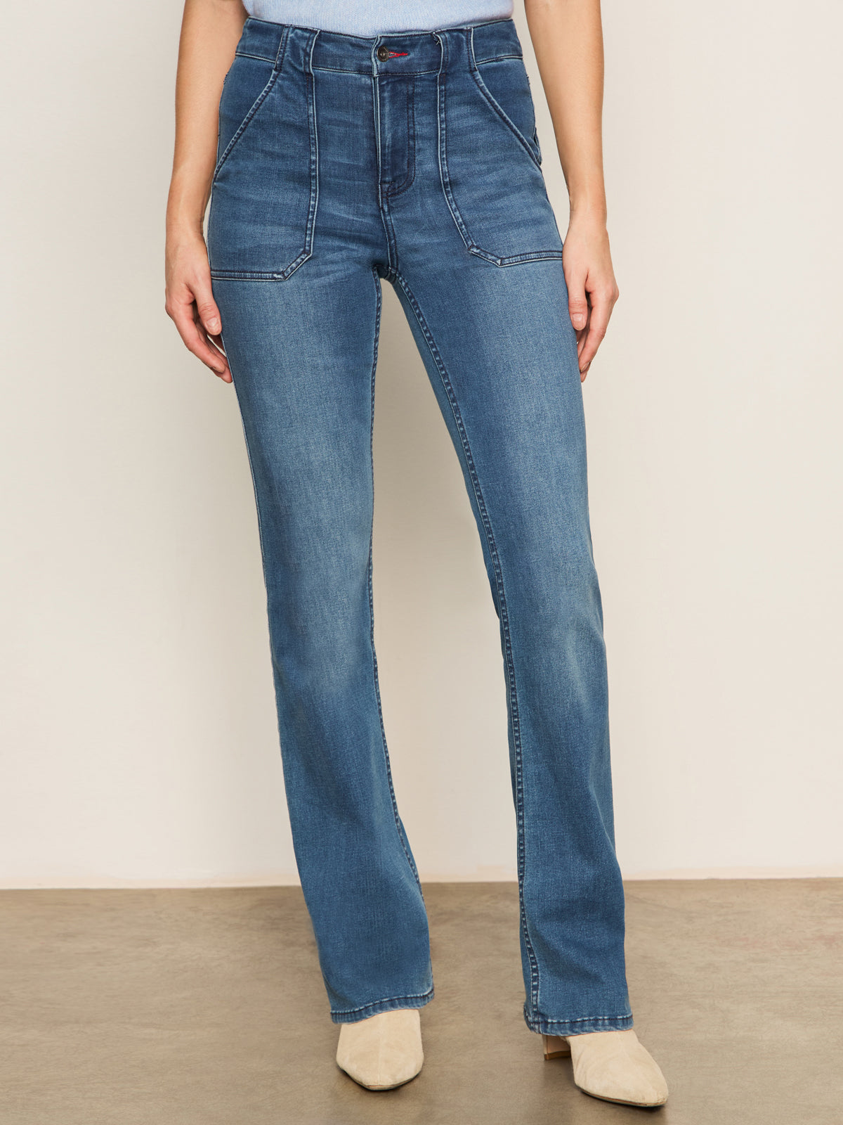 Someone wearing Sanctuary Clothing's Sculpted Hayden Bootcut Lucky Streak jeans stands against a light wall, pairing the high-waisted denim with beige pointed-toe shoes.