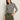 A woman poses against a light background wearing the Sanctuary Clothing boatneck long sleeve tee in light oat black stripe, paired with olive green cargo pants. She has a neutral expression and one hand in her pocket.