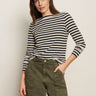 A woman poses against a light background wearing the Sanctuary Clothing boatneck long sleeve tee in light oat black stripe, paired with olive green cargo pants. She has a neutral expression and one hand in her pocket.