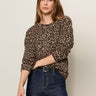 A woman with long brown hair wears the Sanctuary Clothing 24 7 popover french kitty sweater, tucked into high-waisted dark blue jeans, posing against a plain light background.