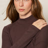 A woman with long brown hair wears the Sanctuary Clothing ls mock essential top in semi sweet, looking at the camera with her left hand on her right shoulder against a neutral background.