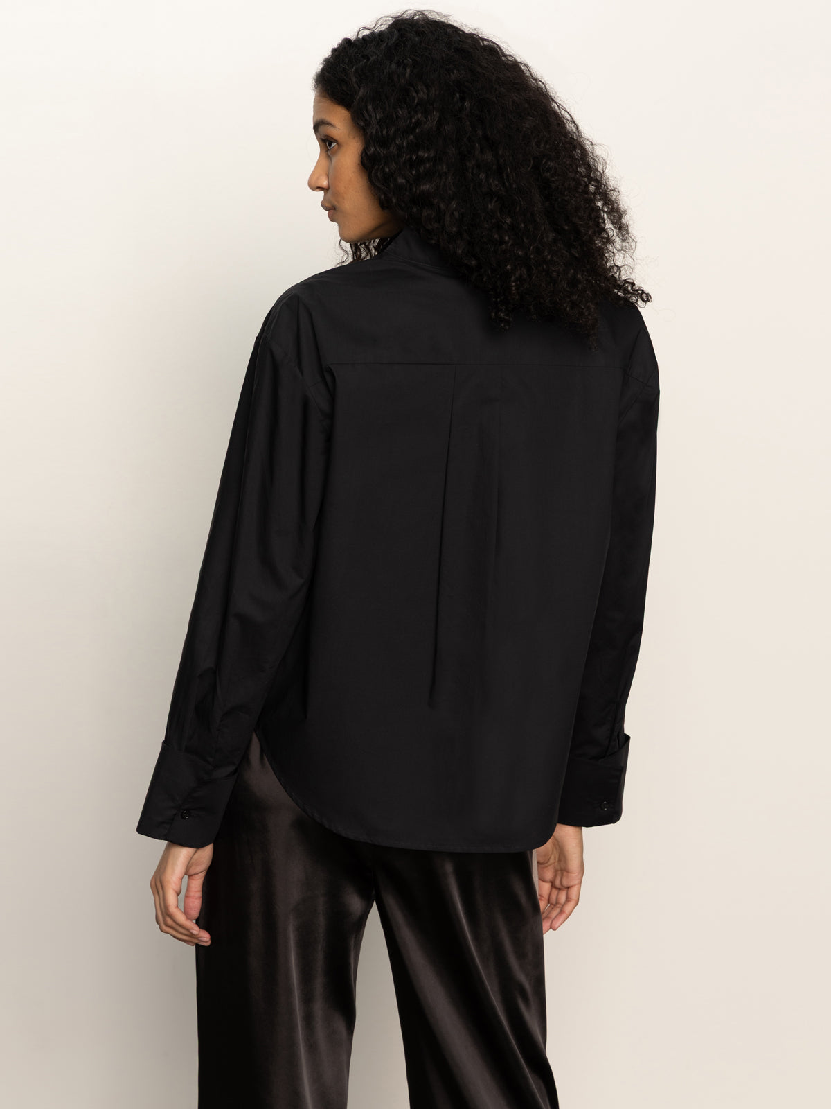 A person with curly hair, facing away from the camera against a plain light background, wears the Sanctuary Clothing new era tuxedo shirt in black.
