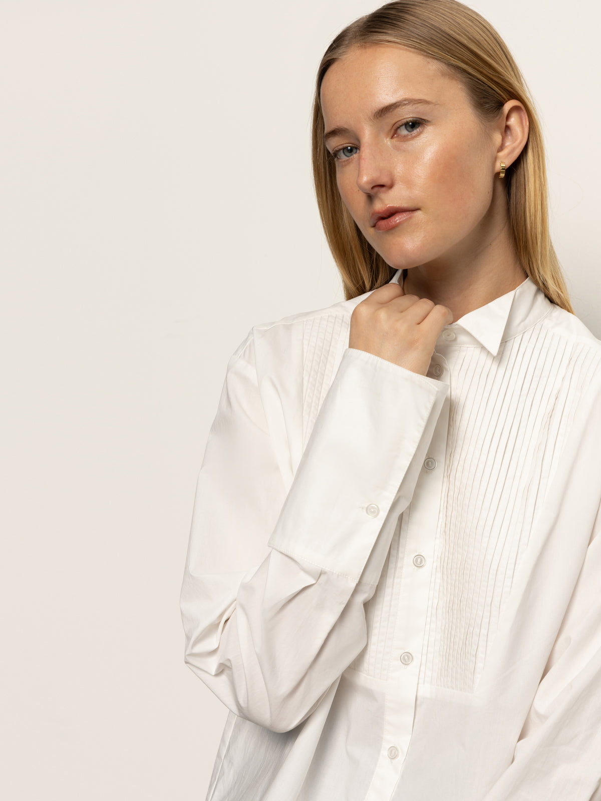 A woman with straight blonde hair wears the Sanctuary Clothing new era tuxedo shirt in white, gazing neutrally at the camera while gently holding the collar, set against a plain light background.