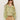 A woman with long brown hair and sunglasses wears the Sanctuary Clothing sheer elegance volume blouse verde boheme, styled with tan high-waisted shorts and a brown belt, standing against a plain background.