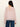 A woman with long dark hair is seen from the back wearing Sanctuary Clothing's Keepsake Volume Blouse in Dried Petal, a sheer light pink, long-sleeve top with a keyhole button and gathered sleeves, paired with blue jeans.