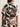 A person is shown from the back wearing Sanctuary Clothing's good time tie shirt lotus in petite sizing, featuring short sleeves and a bold abstract leaf print in black, brown, and cream. Chunky bangles also adorn their wrist.