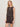 A woman with blonde hair wears the Sanctuary Clothing 'the desired summer crop shell rhythmic,' a sleeveless black romper with a subtle geometric print. She stands against a light background, hand in pocket, accessorized with a necklace.