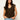 A woman with long, wavy dark hair wears the Sanctuary Clothing outsider embellished shell top in dark cumin black stripe, featuring gold vertical stripes and shoulder details. She stands against a plain light background with one hand in her jeans pocket.