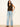 A woman with long dark hair wears the Sanctuary Clothing outsider embellished shell top in dark cumin black stripe, paired with light blue wide-leg jeans and black sandals, standing against a plain white wall.