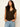 A woman with long wavy hair wears the Sanctuary Clothing Outsider Embellished Shell Top in dark cumin black stripe and light blue jeans, posing against an off-white background with her hands in her pockets.
