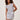 A woman with curly hair models the Sanctuary Clothing side tie t shirt dress in white with navy stripes, featuring a sleeveless design, standing against a plain light-colored wall.