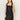 A woman with long brown hair wears the Sanctuary Clothing "almost there linen dress black," a sleeveless style with a square neckline and scalloped hem. She stands against a plain light background, gazing to the side with one hand behind her back.