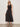 A woman stands against a plain light-colored wall, wearing Sanctuary Clothing's breakaway mix media midi dress in black with sunglasses and black sandals, her hands resting at her sides.