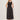 A woman with shoulder-length blonde hair stands by a light wall, wearing Sanctuary Clothing's breakaway mix media midi dress in black and black sandals. The sleeveless dress features a fitted top, button details, and a gathered skirt.