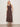 A woman with short blonde hair stands against a plain light wall, wearing Sanctuary Clothing's breakaway mix media midi dress in rich soil. She pairs the sleeveless, buttoned dress with flat sandals and a bracelet for a relaxed, casual look.