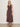 A woman with blonde hair and a relaxed expression wears the Sanctuary Clothing breakaway mix media midi dress in rich soil against a plain background, paired with black flat sandals. The dress is sleeveless, buttoned, and features a gathered skirt.