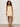 A woman with curly hair wears the Sanctuary Clothing hideaway linen tie strap dress in banana and strappy sandals, accessorized with bracelets on her right wrist, standing confidently against a plain light background.