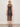 A woman with wavy blonde hair faces away, wearing the Sanctuary Clothing "desire more mesh cinch dress rhythmic," a sleeveless, knee-length sheer black dress with dots. She pairs it with flat sandals and a bracelet against a light background.