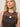 A woman with blonde hair models the sleeveless, patterned brown "desire more mesh cinch dress rhythmic" by Sanctuary Clothing, paired with a necklace featuring a large pink-orange seashell, as she looks slightly up at the camera against a neutral backdrop.