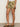 A person stands indoors wearing Sanctuary Clothing's wander on short canyon camo, a white top, and tan crisscross slide sandals. The image is cropped to show only the lower torso and legs.