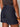 A person in Sanctuary Clothing's "Summit Short First Sight" dark denim shorts with rolled hems, visible stitching, and a branded Sanctuary label pairs them with a patterned black and tan top and chunky brown bangles.