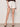A woman models the Summit Short Chalk by Sanctuary Clothing—high-waisted, white denim shorts with front pockets and rolled cuffs—paired with a dark top and beige platform heels against a plain backdrop.