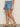 Someone stands against a neutral background wearing Sanctuary Clothing's idyll tie short jean serenade in light blue, paired with a white top and brown strappy flat sandals.