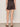 Wearing Sanctuary Clothing's all time linen short rhythmic, a person stands on a concrete floor in brown slide sandals, a black top, and displays a script tattoo on their left forearm. They are shown from the back.