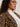 A woman with curly hair and gold-rimmed glasses, wearing Sanctuary Clothing's hometown jacket lynx extended sizing€�a bold leopard print faux fur coat€�over a white shirt, looks confidently to the side.