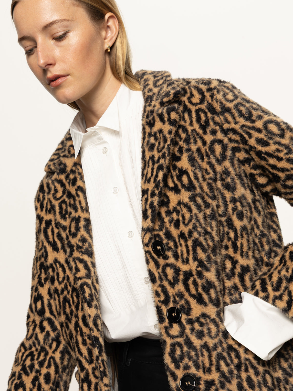 A woman wears the Sanctuary Clothing "hometown jacket lynx," a leopard-print coat with large black buttons, over a white shirt, looking down against a plain white background.