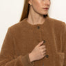 A woman with long blonde hair wears the Sanctuary Clothing "teddy cardi bronze," a brown textured button-up jacket, over a white top, looking left with a neutral expression against a plain white background.