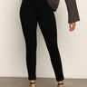 A person models the Sanctuary Clothing runway legging black, paired with a loose dark gray long-sleeve top and black ankle-strap shoes, posed with one hand on their hip against a plain light background, head out of frame.