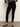 A person stands against a plain background wearing Sanctuary Clothing's runway legging in black, paired with a gray wide-sleeve top and black low-heeled, pointed-toe ankle strap shoes.