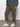 Wearing Sanctuary Clothing's rebel pant hiker green from the inclusive collection, a person stands on a gray floor against a plain white wall, showing only the lower half of their body.