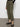A person wearing Sanctuary Clothing's rebel pant hiker green cargo pants with elastic cuffs and black woven Mary Jane shoes stands on a concrete floor against a white wall.