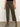 A person wearing Sanctuary Clothing™s marine crop trouser pant fatigue in olive green with front patch pockets, paired with a black top and brown suede heeled ankle boots, stands on a gray floor against a plain light background.
