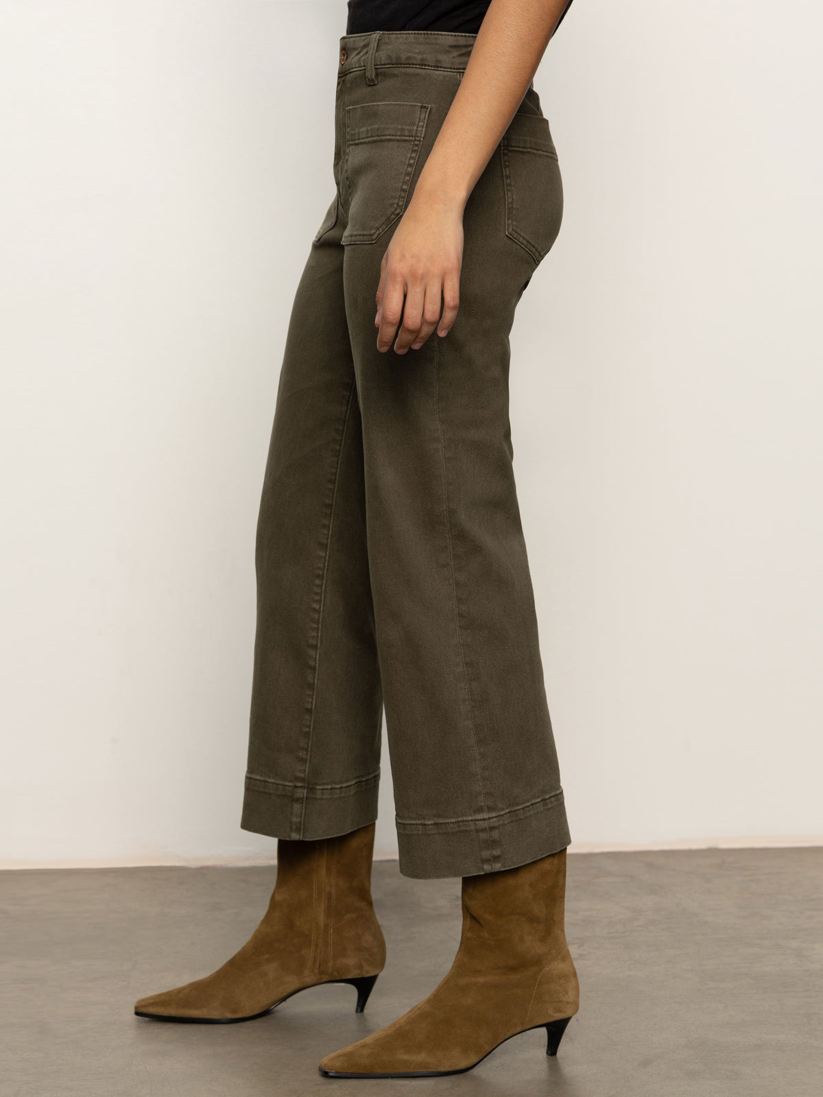 A person stands on a gray floor wearing Sanctuary Clothing's the marine crop trouser pant fatigue in olive-green with tan suede low-heel ankle boots, shown from the side against a plain light background.
