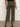 A person stands facing away, wearing Sanctuary Clothing's the marine crop trouser pant fatigue”high-waisted, olive green wide-leg jeans with cuffed hems”and brown heeled boots against a plain background.