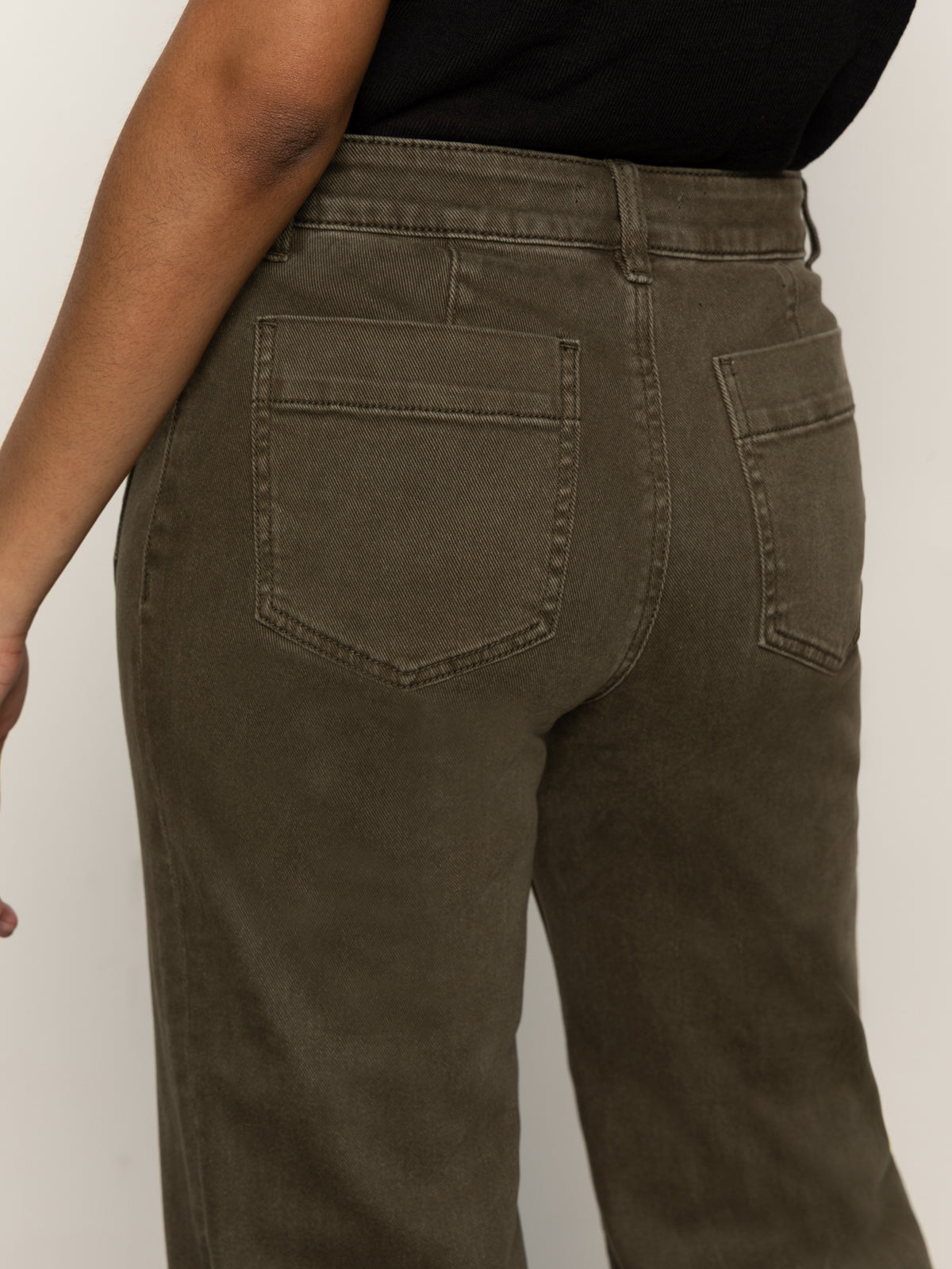 Someone wearing the Sanctuary Clothing marine crop trouser pant fatigue in olive green, a high-waisted style with back pockets, paired with a black top, shown from the waist down and viewed from behind.
