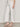 Only the lower half of a person is visible, wearing Sanctuary Clothing's the marine crop jean chalk petite sizing—wide-leg, off-white jeans with a subtle floral pattern—paired with a cream knit top and nude heeled sandals against a light wall.
