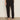 A person wears Sanctuary Clothing's polished cargo pant in black, featuring side pockets and a cropped fit, standing on a brown floor against an off-white wall with black slip-on shoes.