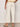 A person faces away, wearing Sanctuary Clothing's soft marine wide leg crop pant collagen in off-white with back pockets, paired with a cream top and beige slide sandals, standing on a light floor against a plain background.