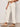A person wearing Sanctuary Clothing's Soft Marine Wide Leg Crop Pant Collagen in off-white, paired with a beige short-sleeve top and tan slide sandals with buckles, stands against a plain background.