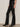 A person models the Sanctuary Clothing slick brook bootcut pant in black, paired with black pointed-toe heels, standing against a plain white wall. Only their lower body is visible.
