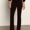 A person indoors wears Sanctuary Clothing„¢s velveteen brook bootcut pant in dark crimson, paired with matching outerwear and heeled ankle boots. Only their lower half is visible against a plain background.