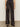 Someone wearing the Sanctuary Clothing modern satin trouser in black, styled with black pointed-toe shoes, stands against a light-colored wall on a neutral floor.