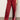 A person wears Sanctuary Clothing's satin track pant crimson€�shiny red with white side stripes and a relaxed fit€�paired with red heeled shoes. The photo, cropped at the torso, highlights the standout pants.