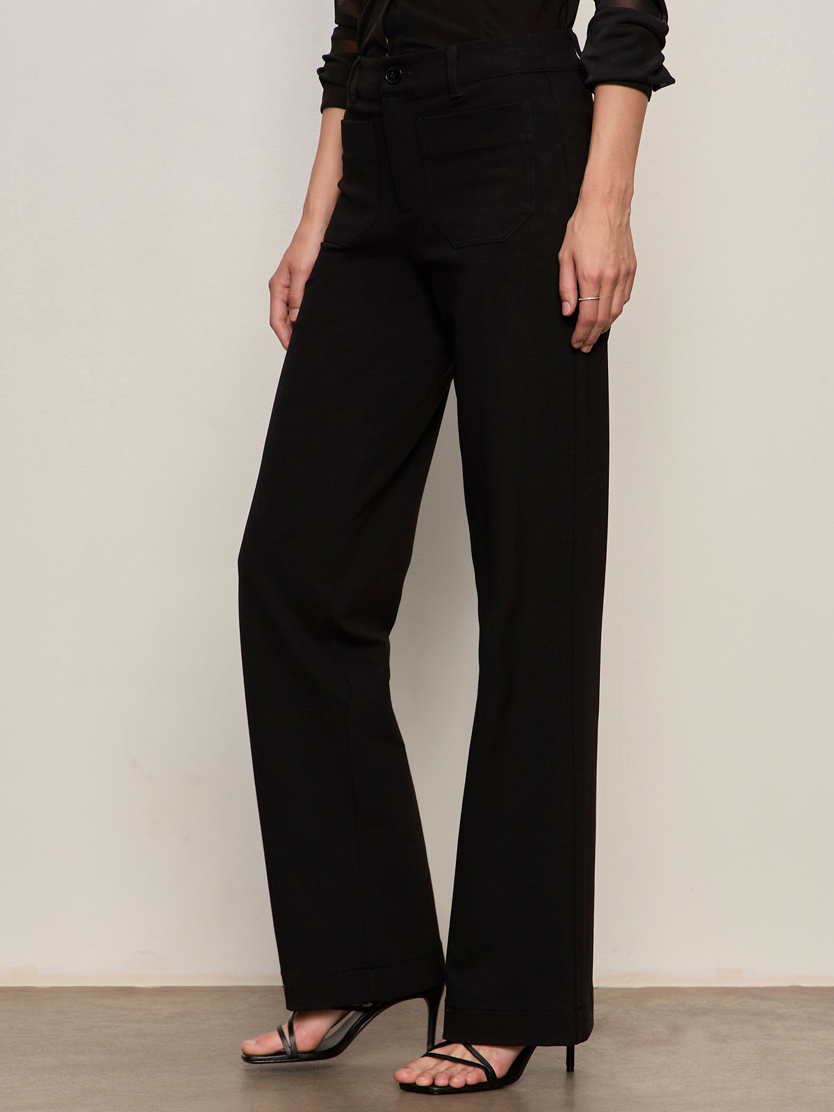A person models the Sanctuary Clothing marine ponte pant in black with black high-heeled sandals, standing against a plain light background; their upper body and face are not shown.