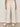Someone wearing the Sanctuary Clothing lily cropped pant in setting sun stripe—cream-colored with thin vertical stripes and a drawstring waist—paired with white sneakers, stands against a plain background.