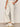 A person stands against a neutral background wearing Sanctuary Clothing's lily cropped pant in setting sun stripe with hands in pockets and white Adidas sneakers featuring beige stripes.